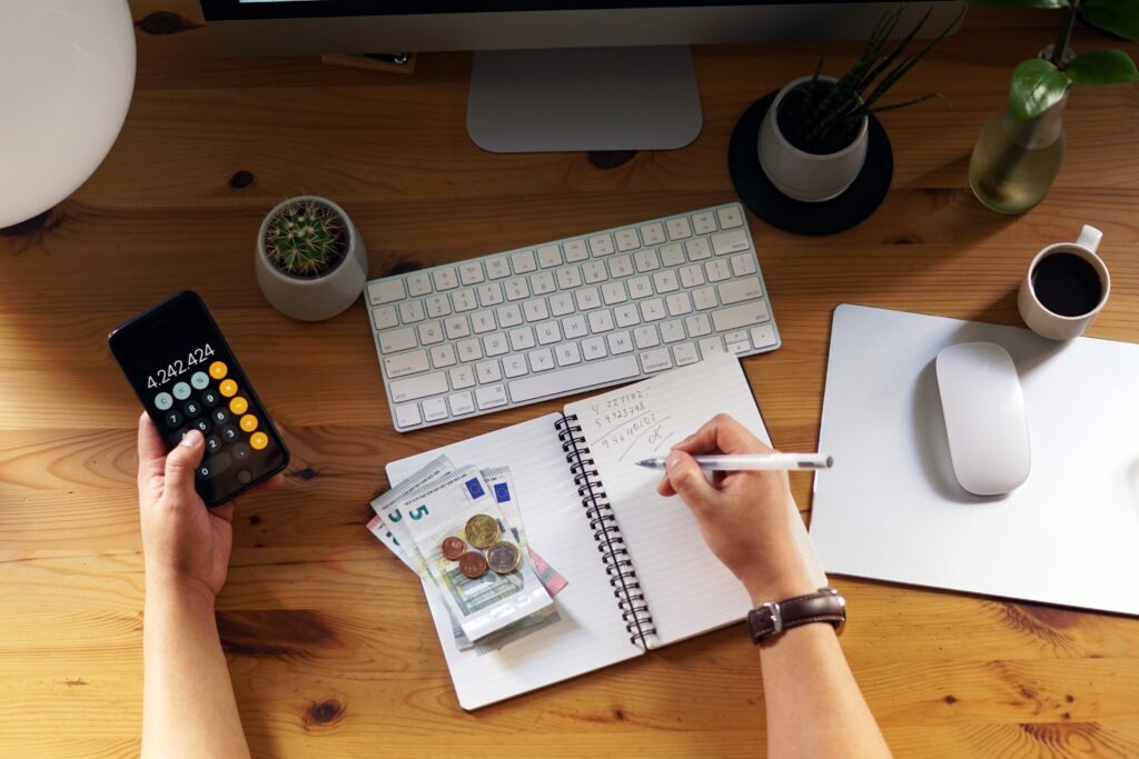 Pessoa organizando as finanças com calculadora, documentos, anotações e computador, representando o planejamento financeiro e a prevenção funeral.