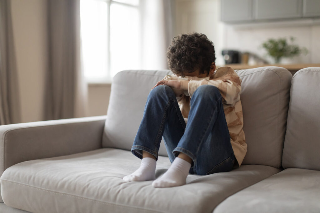 Criança em luto, com a cabeça baixa entre os joelhos, em uma postura introspectiva